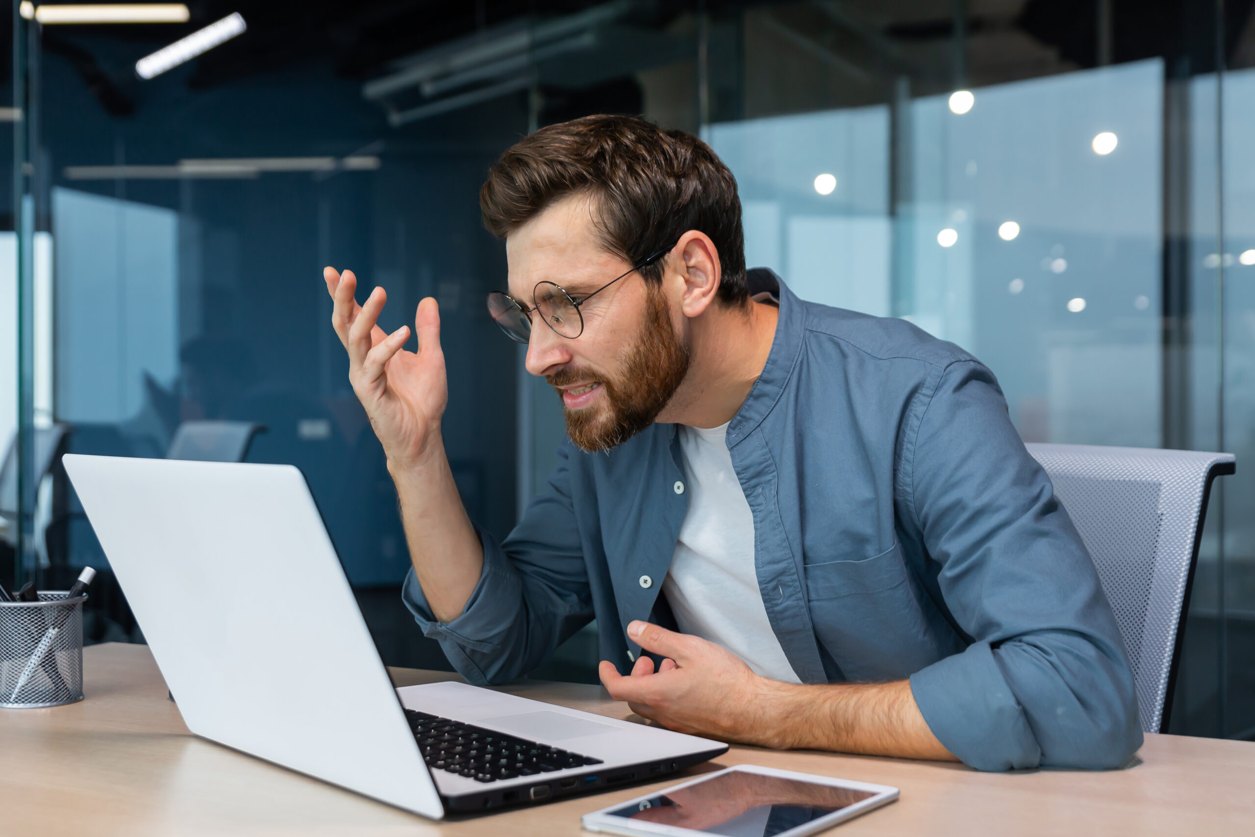 Un hombre de negocios insatisfecho y enojado mirando la pantalla de una computadora portátil, un hombre con camisa informal trabajando dentro de la oficina, empleado molesto
